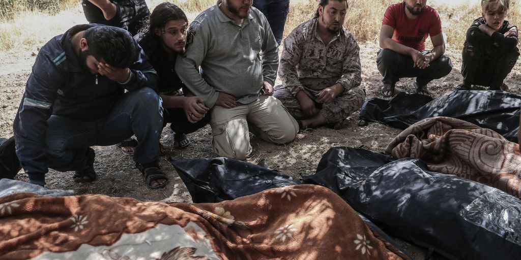 Trauernde sitzen 2021 neben eingehullten leichen unter baumen in idlib und warten darauf dass kampfflugzeuge abziehen